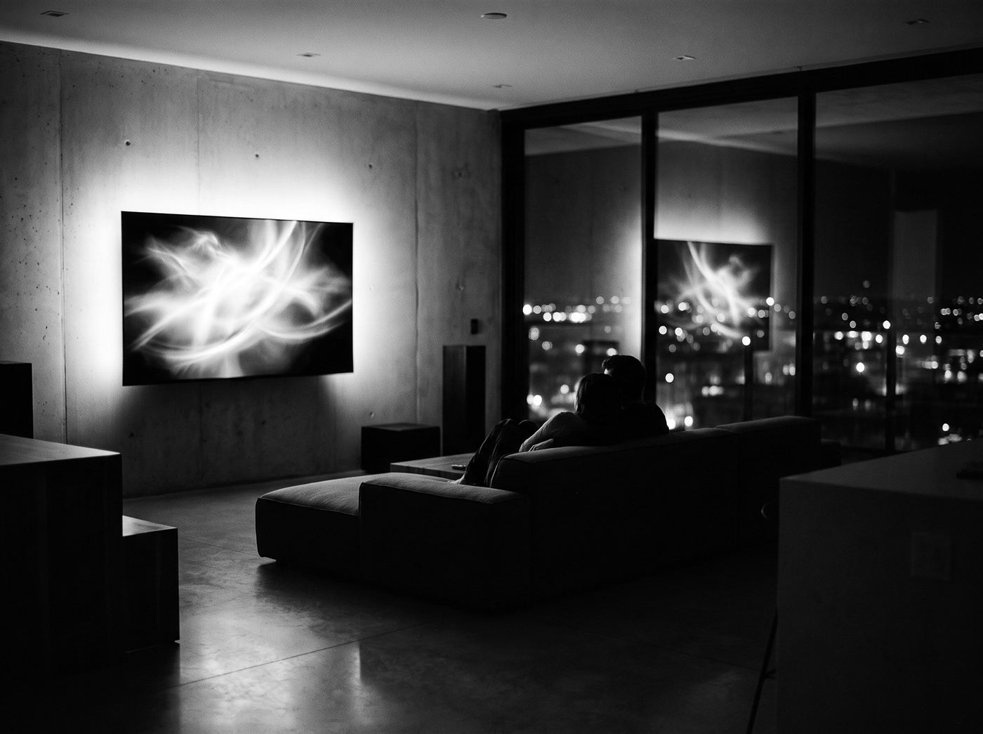 A couple watching a glowing wall-mounted smart TV in a dark modern living room at night