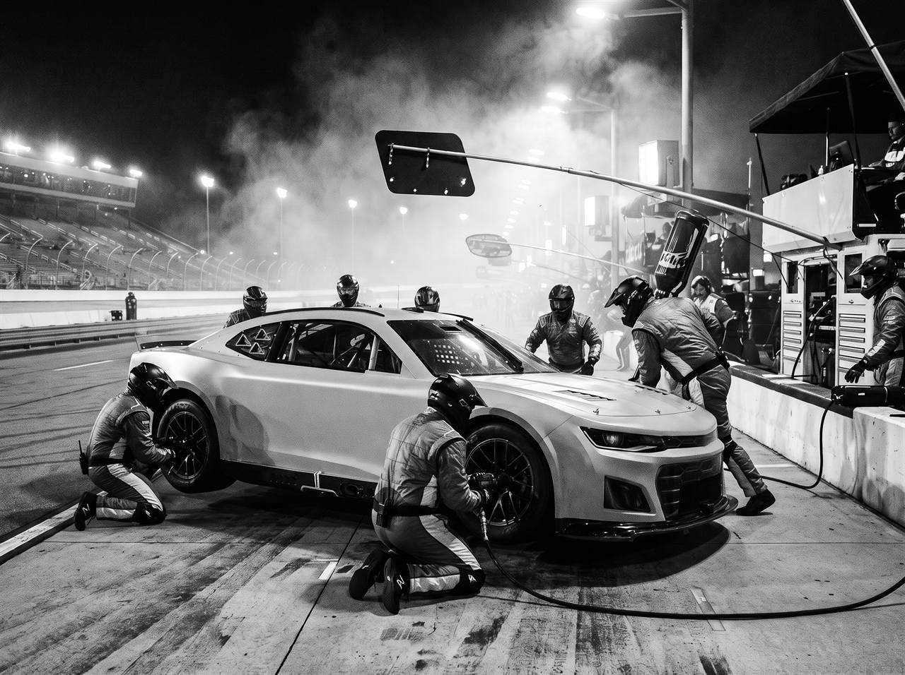 A pit crew changing tires on a NASCAR-style stock car during a night race